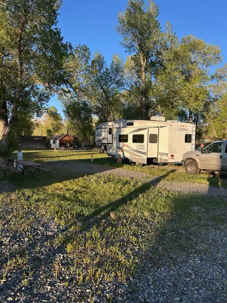 RV parked at Oasis Motel & RV Park with trees and blue sky in background.