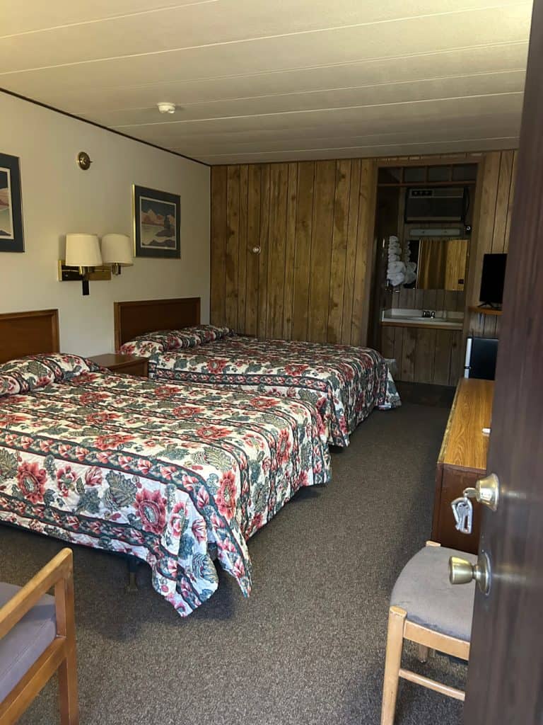Cozy motel room with two beds, wooden wall paneling, and basic amenities in Meeteetse, Wyoming.
