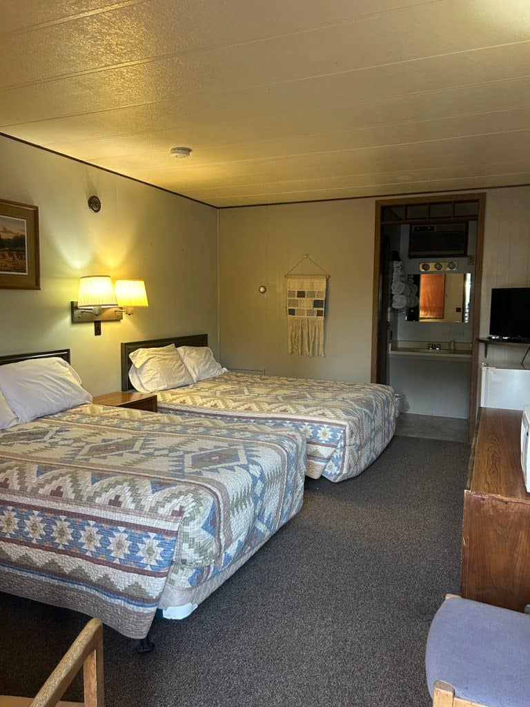Interior view of a motel room with two beds, lamps, and a small TV in Meeteetse, Wyoming.